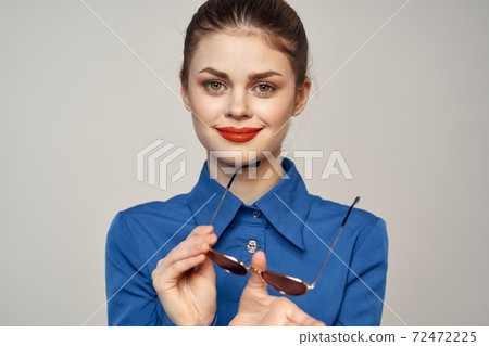 Fashionable woman in sunglasses and a blue shirt gesturing with her hands on a light background cropped view 72472225