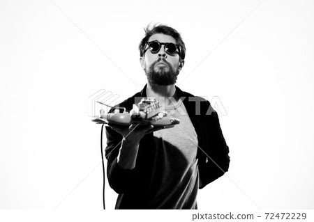 A man holds a guitar in his hands black leather jacket dark glasses music performance light background 72472229