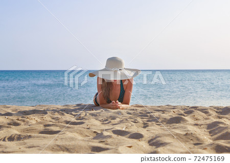 journey to the sea. girl in a bathing suit and hat sunbathing on the beach. tourist sitting on the sand. leisure wear. copy space 72475169