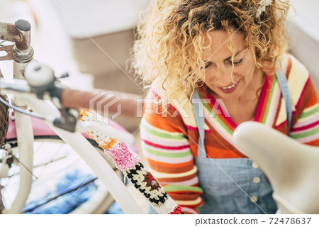 Close up portrait of cheerful beautiful caucasian middle age blonde woman at home working on a coloured bike - home activity work for happy and alternative people 72478637