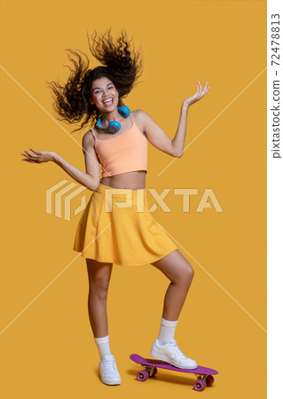 Pretty dark-haired young girl with a skateboard looking joyful Pretty dark-haired young girl with a skateboard looking joyful 72478813