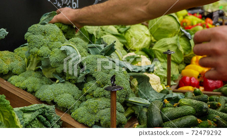 Close-up hands of grocery worker is arranging vegetables on store shelves. Close-up hands of grocery worker is arranging vegetables on store shelves. 72479292