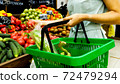 Woman with shopping basket is choosing vegetables in grocery store. 72479294