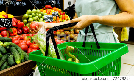 Woman with shopping basket is choosing vegetables in grocery store. Woman with shopping basket is choosing vegetables in grocery store. 72479294