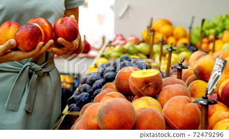 Young caucasian woman is choosing a nectarines at supermarket Young caucasian woman is choosing a nectarines at supermarket 72479296