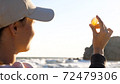 Young woman is holding seashell in hand and looking on sun through shell 72479306