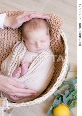 Cute little baby in a knitted hat with a toy bunny lies in a wicker basket decorated with greens and lemons in a beige knitted blanket. Summer mood. Happy healthy childhood Cute little baby in a knitted hat with a toy bunny lies in a wicker basket decorated with greens and lemons in a beige knitted blanket. Summer mood. Happy healthy childhood 72479975