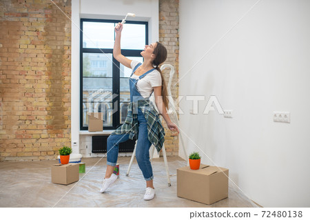 Young woman with paint roller in her hand feeling cheerful Young woman with paint roller in her hand feeling cheerful 72480138