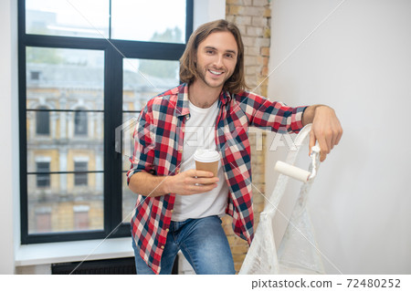 Young man standing near the stepladder and having cofee Young man standing near the stepladder and having cofee 72480252