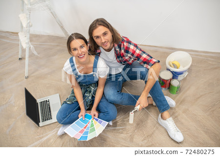 Young couple sitting on the floor and choosing a color for paint 72480275