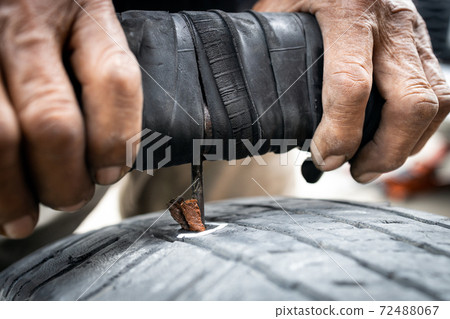 Patch a tyre,Hands of old man patching puncture tubeless car tire,repair rubber surface that have been stabbed by nails,recap on the tire tread,stabbing rubber patch needle and glue into the puncture 72488067