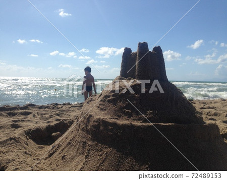 Boy looking at the sea near the sand castle Boy looking at the sea near the sand castle 72489153