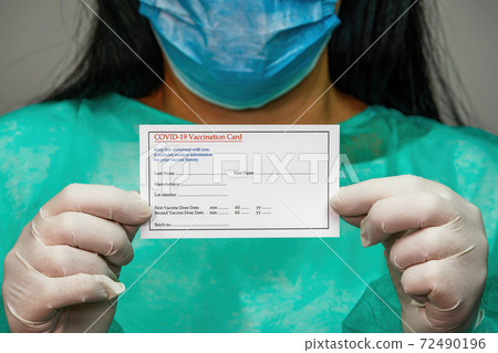Chemist with protective suit holds a covid-19 vaccination card. 72490196