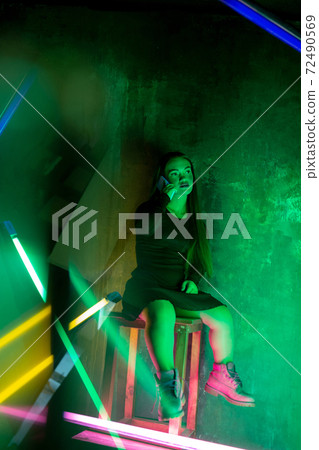 Caucasian female inclusive model posing on studio background in neon light 72490569