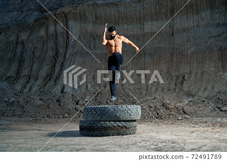 Handsome strong man jumping on wheel during evening workout Handsome strong man jumping on wheel during evening workout 72491789