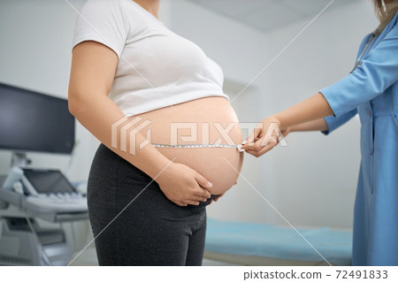 Doctor using measuring tape while examining woman's belly 72491833