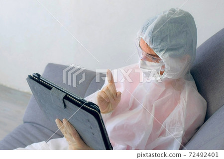 Woman in protective suit, mask, glasses, gloves talking video chat on tablet. 72492401