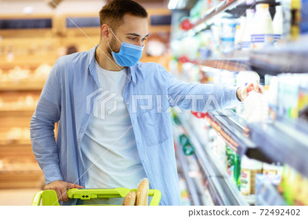 Man in medical mask shopping in supermarket taking milk Man in medical mask shopping in supermarket taking milk 72492402