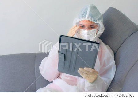 Woman in protective suit, mask, glasses, gloves talking video chat on tablet. Woman in protective suit, mask, glasses, gloves talking video chat on tablet. 72492403
