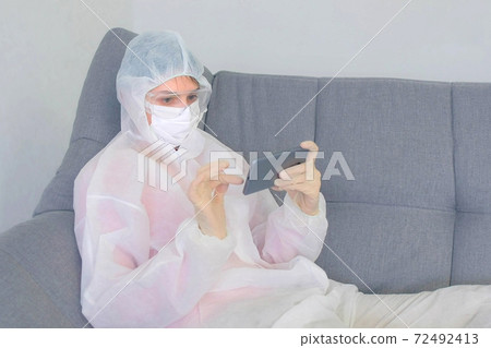Woman in protective suit is browsing smartphone on coronavirus quarantine. Woman in protective suit is browsing smartphone on coronavirus quarantine. 72492413