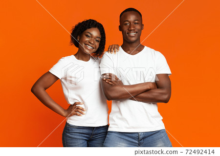 Smiling black couple posing together on orange background Smiling black couple posing together on orange background 72492414