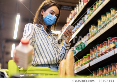 Woman in mask using smartphone standing in store 72492453
