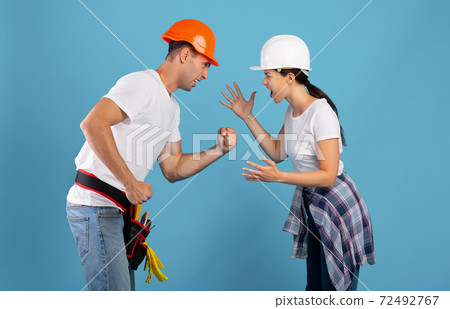 Renovation And Conflicts. Young couple in hard hats arguing during house repair Renovation And Conflicts. Young couple in hard hats arguing during house repair 72492767