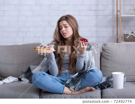 Eating disorders concept. Stressed young woman devouring sweets on couch at home, full length portrait Eating disorders concept. Stressed young woman devouring sweets on couch at home, full length portrait 72492774