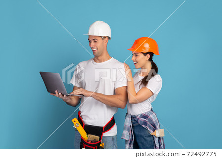 Young couple in hardhats using laptop during house repair, blue background Young couple in hardhats using laptop during house repair, blue background 72492775