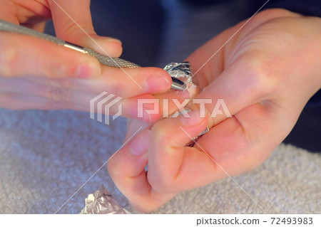 Woman is removing gel polish shellac from nails using pusher, manicure at home. Woman is removing gel polish shellac from nails using pusher, manicure at home. 72493983