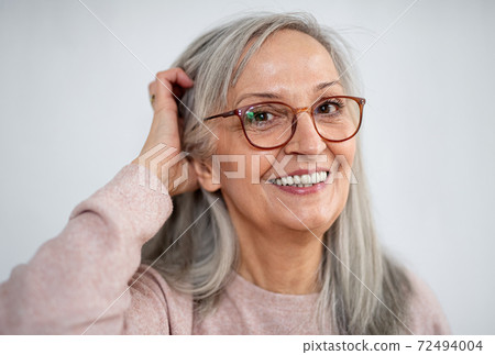 Portrait of senior woman standing indoors against light background, looking at camera. Portrait of senior woman standing indoors against light background, looking at camera. 72494004