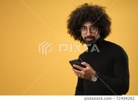Portrait of mature man with smartphone in a studio on yellow background. 72494262