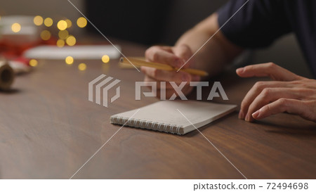 man writes christmas gift list for holidays in notepad with a pencil under warm light in the evening man writes christmas gift list for holidays in notepad with a pencil under warm light in the evening 72494698