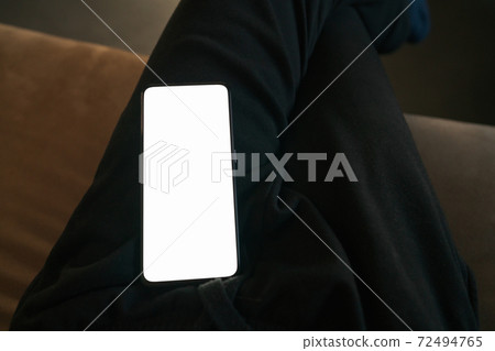POV photo of man sitting on a couch with smartphone on his knees 72494765