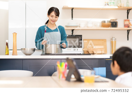 一位母親在廚房做飯，一個男孩在桌旁上在線課 72495332