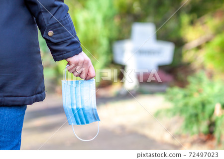 Woman, standing at the grave of family members with a facemask during the pandemic 72497023