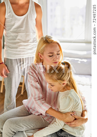 a woman sits with a child, calms her down while a man swears at them a woman sits with a child, calms her down while a man swears at them 72497285