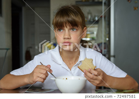 Girl thoughtfully eats soup at the table in the kitchen Girl thoughtfully eats soup at the table in the kitchen 72497581