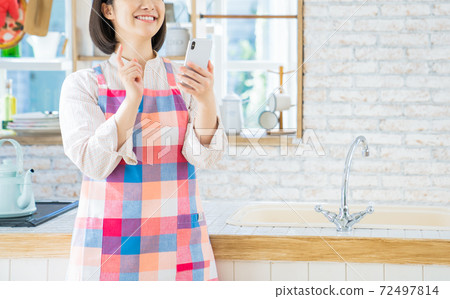 A young woman using a smartphone in the kitchen 72497814