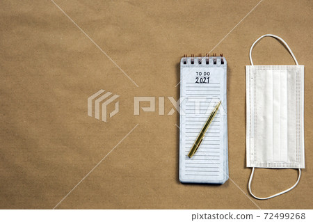Notepad with to do measures for 2021 Coronavirus, Covid-19 written on with gold pencil, top view on brown paper background texture, virus and New Year concept 72499268