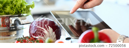 Young man cooking fresh salad and using tablet computer 72500056
