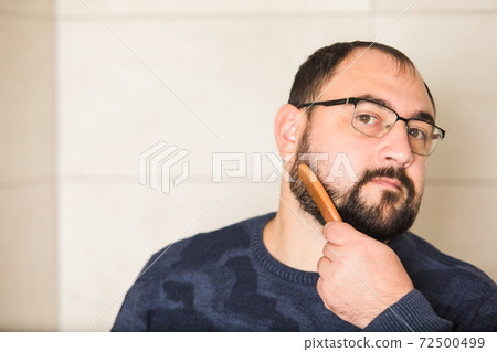 Young man comb his beard and moustache and look Young man comb his beard and moustache and look 72500499