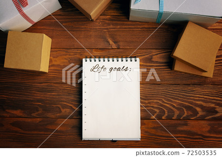 Wooden table with gift boxes notepad with list of life goals. Wooden table with gift boxes notepad with list of life goals. 72503535