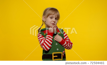 Shy shamed child girl in Christmas elf Santa helper costume posing looking camera, blows air kiss Shy shamed child girl in Christmas elf Santa helper costume posing looking camera, blows air kiss 72504481