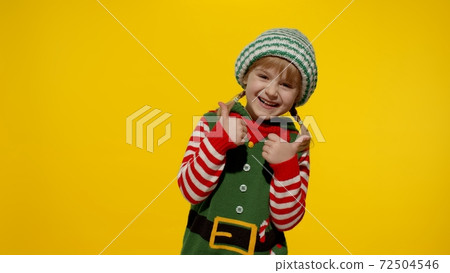 Kid girl child in Christmas elf Santa helper costume showing thumbs up gesture. New Year holiday Kid girl child in Christmas elf Santa helper costume showing thumbs up gesture. New Year holiday 72504546