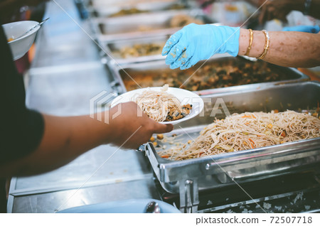 The hand of the wanderer extends to receive food from donations. With volunteers scooping food The hand of the wanderer extends to receive food from donations. With volunteers scooping food 72507718