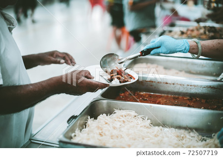 The hand of the wanderer extends to receive food from donations. With volunteers scooping food The hand of the wanderer extends to receive food from donations. With volunteers scooping food 72507719