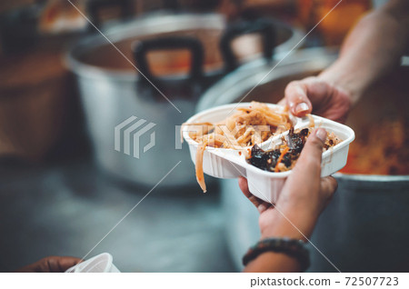 The hand of the wanderer extends to receive food from donations. With volunteers scooping food The hand of the wanderer extends to receive food from donations. With volunteers scooping food 72507723
