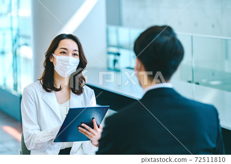 Occupational physician woman in a mask counseling a businessman in a suit at the company Occupational physician woman in a mask counseling a businessman in a suit at the company 72511810