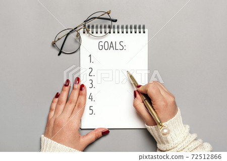 female hand holds pen and writes text 2021 New Year goals on white notepad on gray background Top view Flat lay Business motivation, idea, success, vision, inspiration, planning concept Mock up 72512866